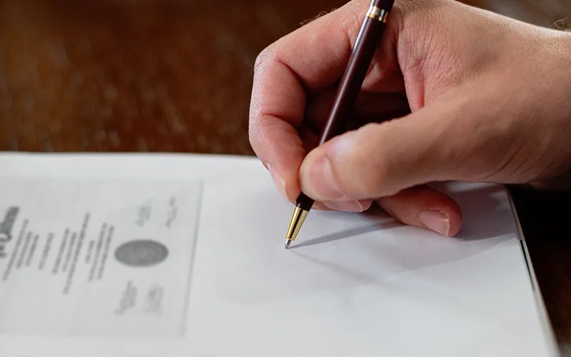 Mano firmando un documento oficial con un bolígrafo dorado