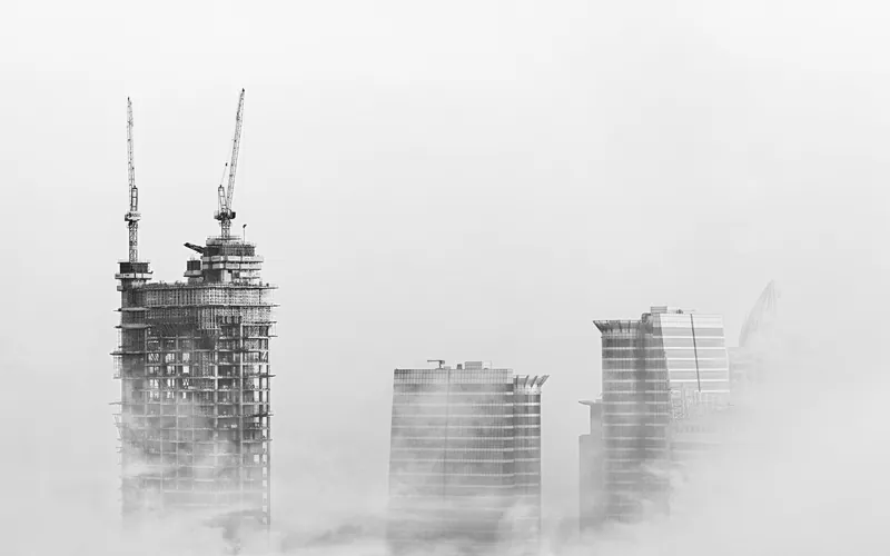 Towers under construction and cranes in Dubai rising through fog