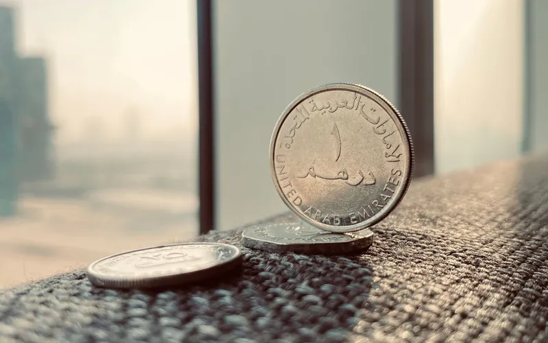 Monedas de un dírham junto a una ventana con los rascacielos de Dubái al fondo